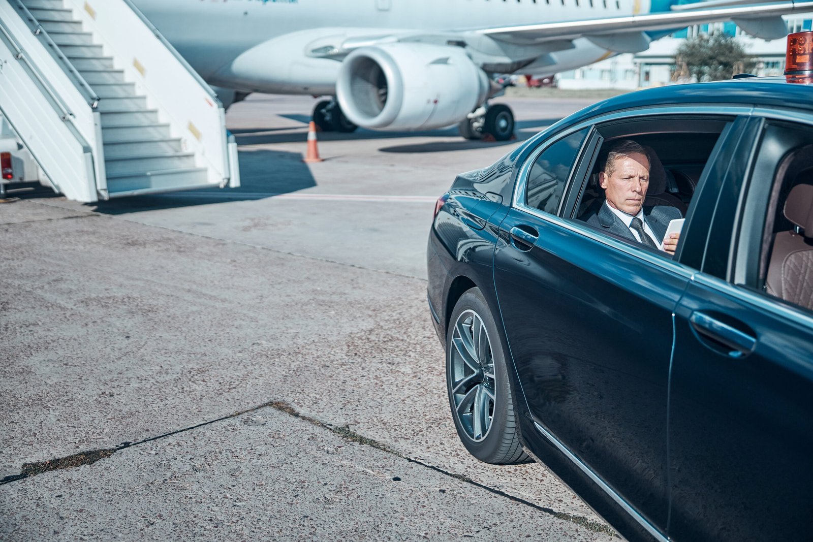 Professional chauffeur waiting by a black luxury sedan at an airport for a Logan Airport limo transfer.