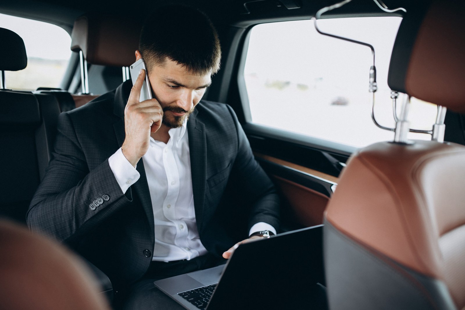 Businessman working on a laptop in the back of a Chauffu executive black car in Boston.