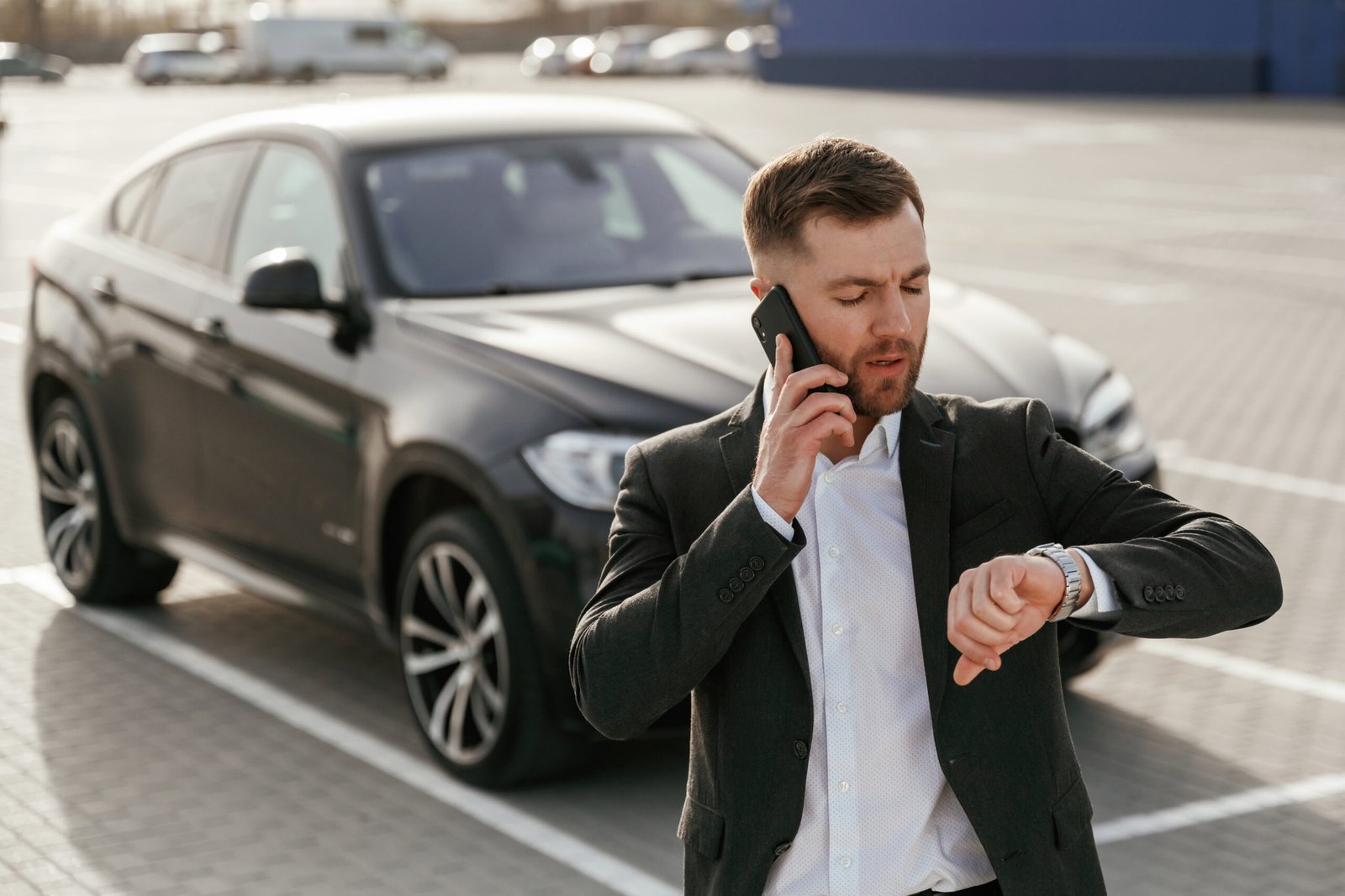 Professional chauffeur in a suit checking his watch next to a luxury black car for hourly limo service in Boston.